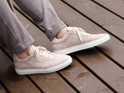 Person wearing light beige sneakers and light gray pants standing on a wet wooden deck.
