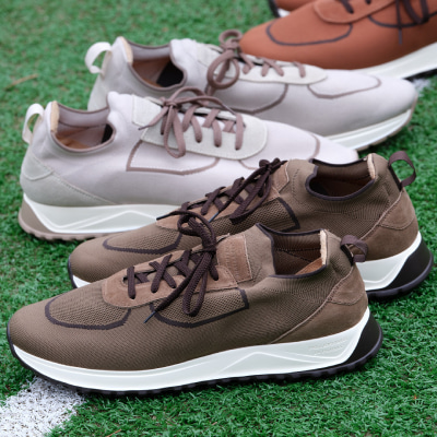 Three pairs of athletic sneakers in brown, gray, and beige are displayed on a green turf surface, positioned in a diagonal arrangement.